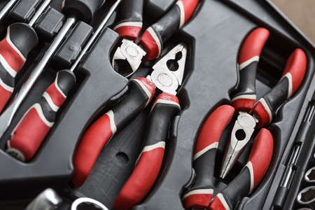 Black-red pliers and screwdrivers in the dark toolbox. Closeup top view photo. Horizontal.の写真素材