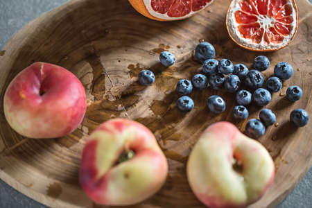 Multicolored fruit on the textured wooden board on the gray surface. There is a heap of blueberries, three peaches and a sliced grapefruit. Closeup. Horizontal.の写真素材