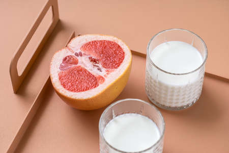 Pair of glasses with milk and a juicy grapefruit on the orange metal support on the same table in the studio. Closeup. Horizontal.の写真素材