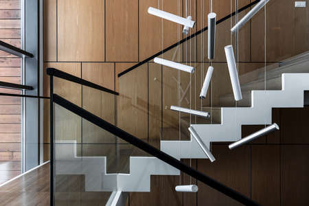 Interior in a modern style with wooden walls and a stair with wooden rungs and glass railing. There are hanging fancy lamps. Horizontal.の写真素材