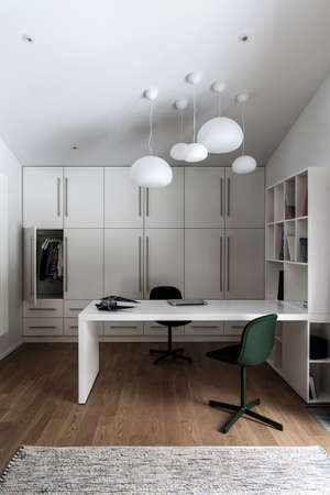 Kid's room with white walls and a parquet with a carpet on a floor. There is a white table with shelves, lockers, black and green chairs, hanging fancy lamps. Vertical.の写真素材