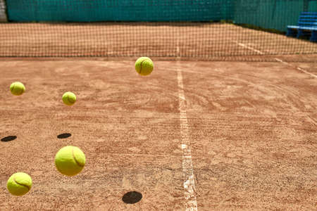Several jumping yellow tennis balls on the court outdoors. Sun shines on them so they drop shadows. Horizontal.の写真素材