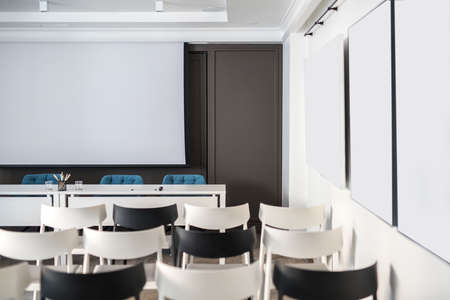 Comfortable conference hall with white walls. There are many light and dark chairs, board, tables...
