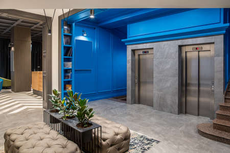 Amazing hallway in the hotel with blue walls and a tiled floor. There are two lifts, brown stair,...