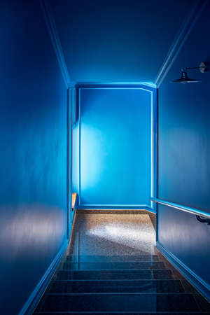 Glossy tiled stair with a handrail in the hotel with blue walls. There is a window and a hanging metal lamp on the right wall. Vertical.の写真素材
