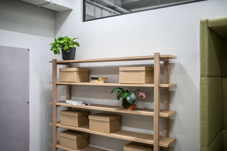 Luminous interior in an office with gray walls. There are wooden shelves with cardboard boxes and green plants and books, board and wide mirror on the walls. Horizontal.の写真素材