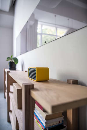 Wooden shelves on the gray wall background in the office. On them there is an yellow speaker, green plant, books and cardboard boxes. Over the shelves there are glossy boards. Closeup. Vertical.の写真素材