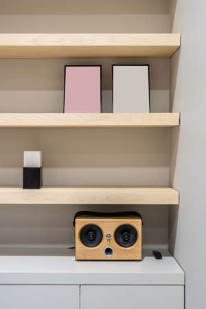 Light wooden shelves on the gray wall background in a luminous office. There is a speaker with a black remote controller, frames, lockers. Closeup. Vertical.の写真素材
