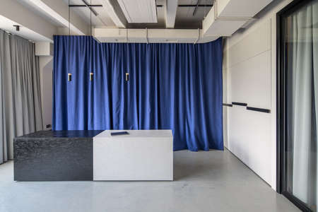 Interior in an office in a loft style with gray walls. There is a textured black-white reception desk with a laptop, multicolor curtains, glass door, hanging lamps. Horizontal.の写真素材
