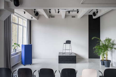 Amazing conference hall with gray walls and a glossy floor. There are multicolor chairs, metallic blue stand, green plants in the pots, window with curtains, lamps and speakers. Horizontal.の写真素材