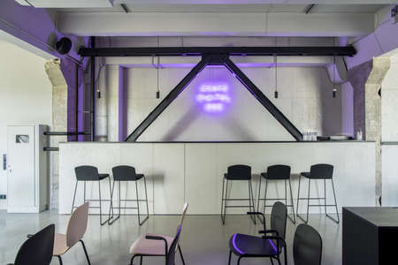 Trendy bar with a rack and black wooden partitions in an interior in a loft style with gray walls and concrete columns. There are different chairs, glasses and faucet on the rack, hanging lamps.の写真素材