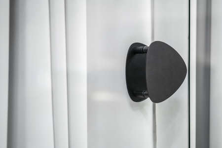 Glass door with a black handle on the gray curtains background in a luminous interior. Closeup low aperture photo. Horizontal.の写真素材