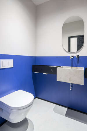 Nice restroom in an office with multicolored walls. There is a white toilet, black rack with a concrete sink, chrome faucet, mirror. Vertical.の写真素材