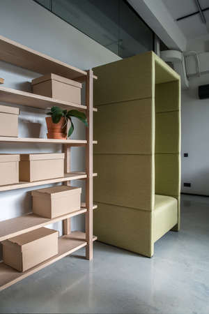 Stylish office in a loft style with gray walls and a glossy floor. There are wooden shelves with cardboard boxes and a plant in an orange pot, fancy green armchair. Vertical.の写真素材