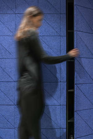 Textured blue wall with an opened door to the black shelves in a luminous interior. There is a woman...