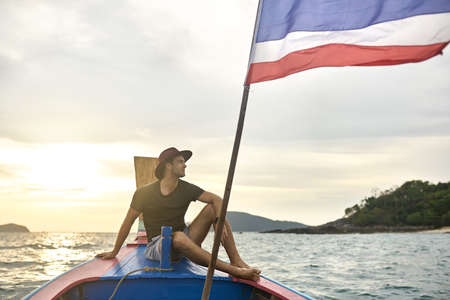 Tanned man with stubble is sailing on colorful boatの写真素材