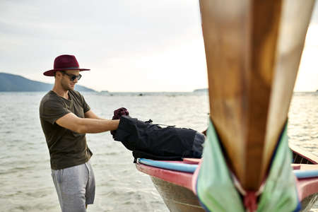 Man with stubble with black backpack near wooden boatの写真素材