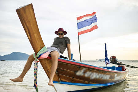 Tanned man with stubble is sailing on colorful boatの写真素材