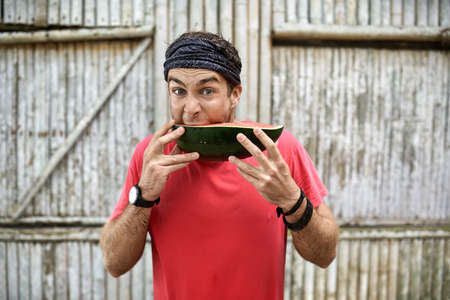 Man with stubble with funny facial expression is eating watermelonの写真素材