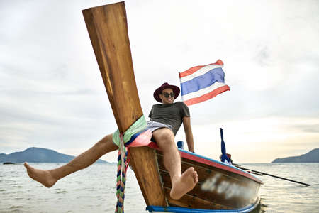 Tanned man with stubble is sailing on colorful boatの写真素材