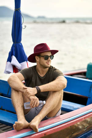 Tanned man with stubble is sailing on colorful boatの写真素材