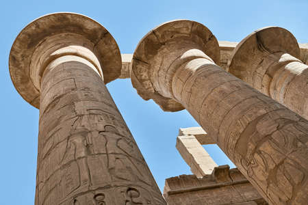 Ancient columns with egyptian hieroglyphs on the blue sky background in Karnak Temple in Egypt. Sun shines onto them. Horizontal.の写真素材