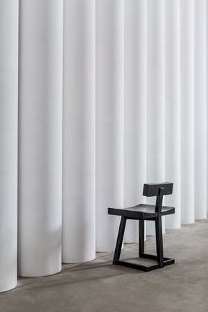 Stylish dark wooden chair on the concrete floor on the background of the white textured columns. Closeup. Vertical.の写真素材
