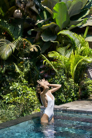 Brunette girl in swimsuit posing in outdoor pool on sunny nature backgroundの写真素材