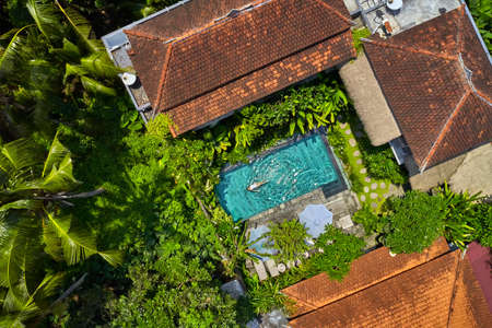 Houses with colorful shingle roofs and pool with swimming woman between palm treesの写真素材
