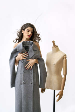 Model covers her body with gray coat near sewing mannequinの写真素材