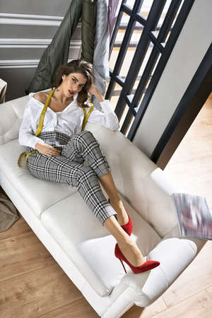 Fashion designer with measuring tape on light sofaの写真素材