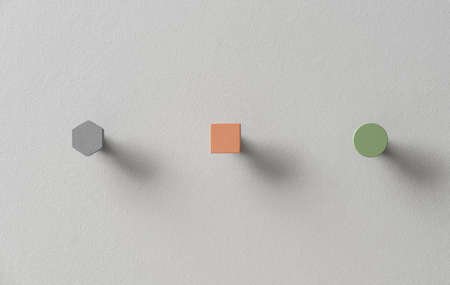 Metal hangers in forms of gray hexagon and orange square and green circle on light wall in studioの写真素材