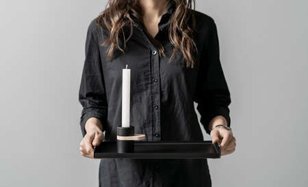 Girl in dark shirt holding metal black tray with candlestick on gray backgroundの写真素材