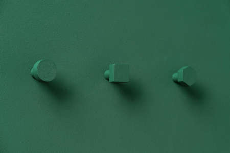 Nice metal dark green geometric hangers on the same color textured wall indoors. They are round, square and hexagon. Closeup horizontal photo.の写真素材