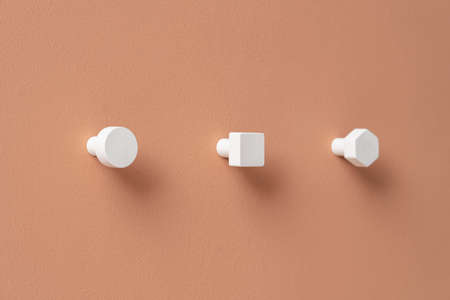 Beautiful metal white geometric hangers on the textured orange wall indoors. They are round, square and hexagon. Closeup horizontal photo.の写真素材