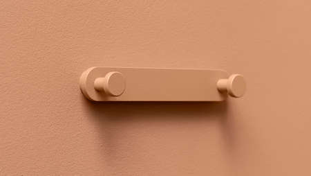 Metal coral hanger on the same color textured wall indoors. Closeup horizontal photo.の写真素材