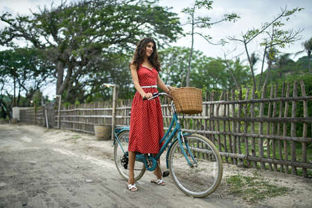 Joyful woman posing with her bicycle on country road on tropical nature backgroundの写真素材