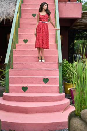 Brunette woman in red dress posing on colorful vintage stair outdoorsの写真素材