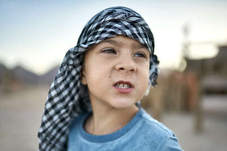 Small boy in checkered keffiyeh grimacing outdoorsの写真素材