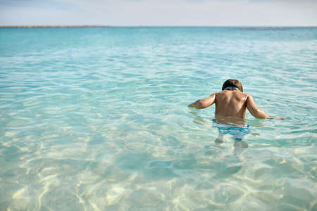 Tanned kid swimming in sea on sunny sky background