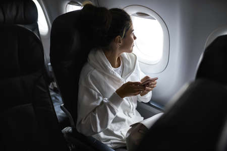 Woman with smartphone sits on black seat in planeの写真素材