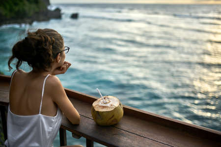 Woman in glasses looking at sunset sea in outdoor cafeの写真素材