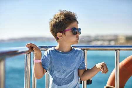 Small boy in sunglasses eating lollipop on yacht deckの写真素材