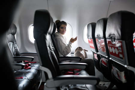 Woman with smartphone sits on black seat in planeの写真素材