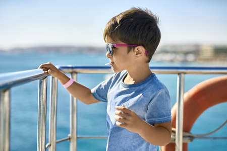 Small boy in sunglasses eating lollipop on yacht deckの写真素材