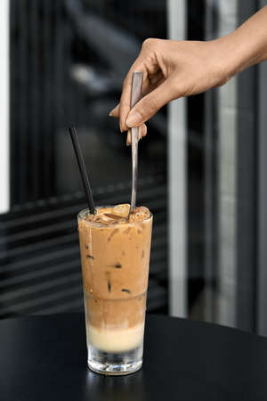 Girl stirs iced coffee drink with spoon in outdoor cafeの写真素材