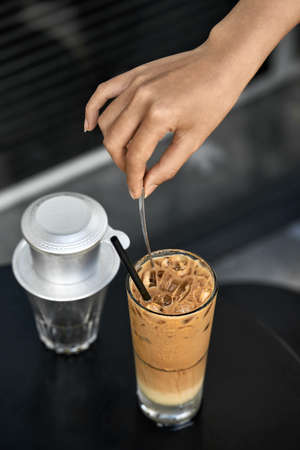 Girl stirs iced coffee drink with spoon in outdoor cafeの写真素材