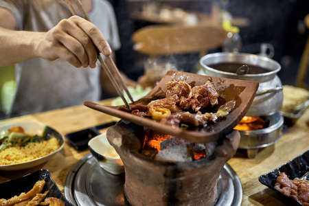 Visitor of traditional vietnamese restaurant cooking meat on hot potの写真素材