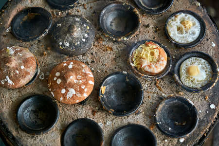 Tasty scrambled eggs and shrimps are roasting in the black bowls on the stone clay BBQ on the street market in Vietnam. Some of bowls covered with brown caps. Top view closeup photo. Horizontal.の写真素材
