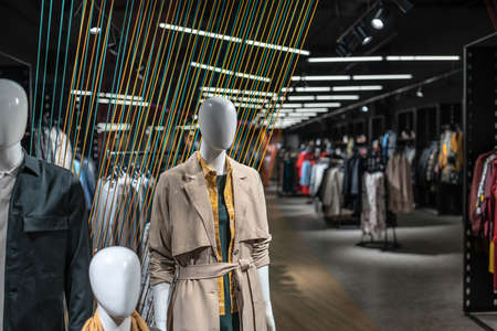 Family of mannequins in casual clothes stands in a big luminous clothing store with dark walls and multicolored ropes lines installation. There are many hangers with different wear. Horizontal.の写真素材